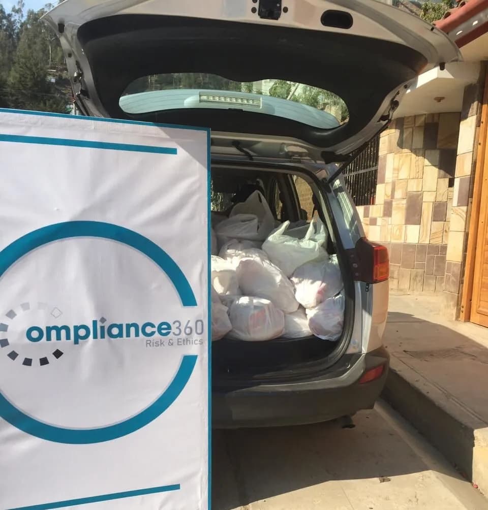 Bolsas de víveres cargadas en el baúl de una camioneta, con el cartel de Compliance360